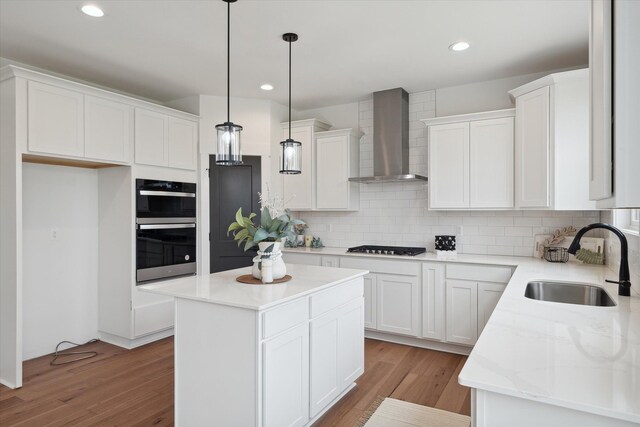 kitchen featuring wall chimney exhaust hood, sink, a center island, double oven, and white cabinets