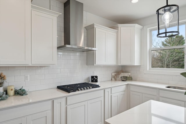 kitchen with pendant lighting, wall chimney exhaust hood, tasteful backsplash, white cabinets, and stainless steel gas stovetop