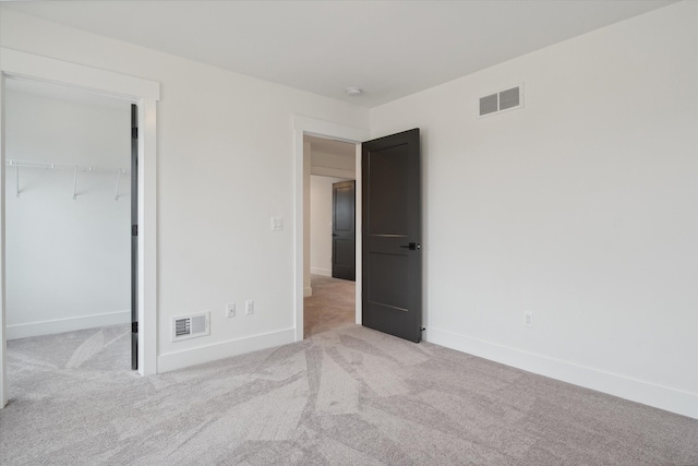 unfurnished bedroom featuring a walk in closet, light carpet, and a closet