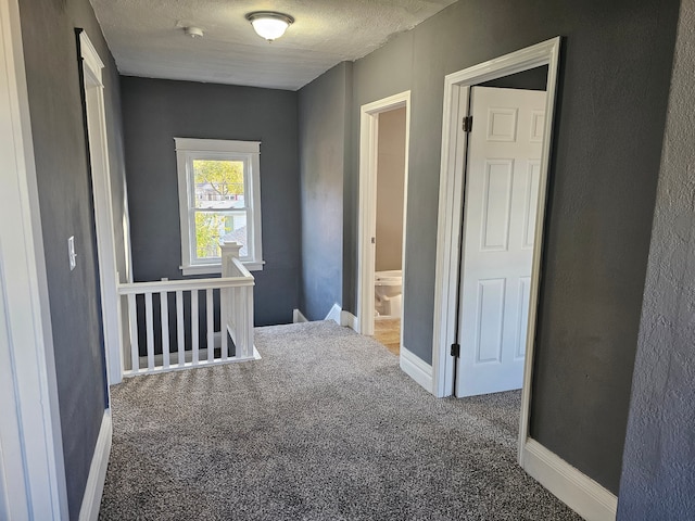 corridor featuring dark carpet and a textured ceiling