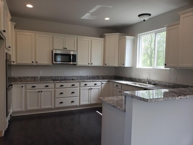 kitchen featuring stone counters, white cabinets, dark hardwood / wood-style flooring, kitchen peninsula, and stainless steel appliances