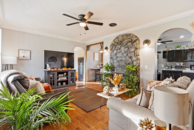 living room with a textured ceiling, ceiling fan, light wood-type flooring, and crown molding