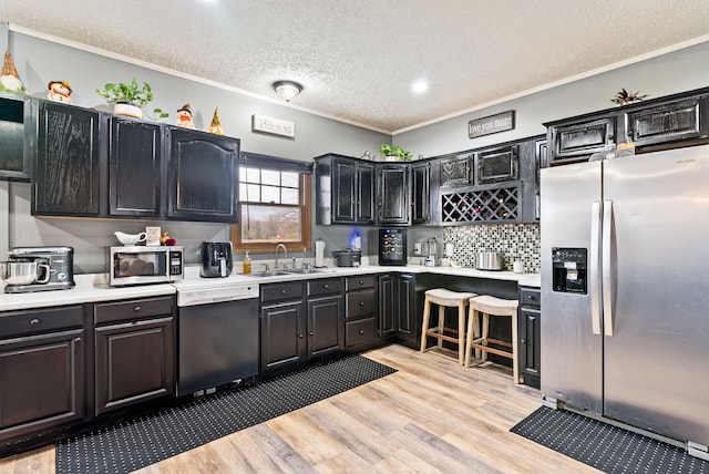 kitchen with sink, crown molding, a textured ceiling, appliances with stainless steel finishes, and light wood-type flooring