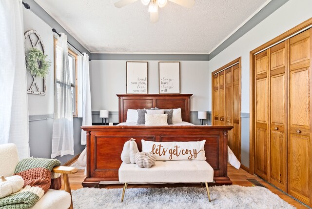 bedroom with light hardwood / wood-style flooring, ceiling fan, ornamental molding, a textured ceiling, and multiple closets