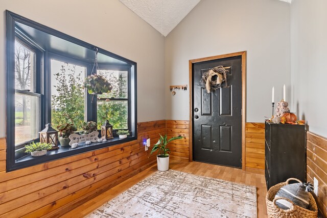 entrance foyer featuring vaulted ceiling, a wealth of natural light, and wood walls