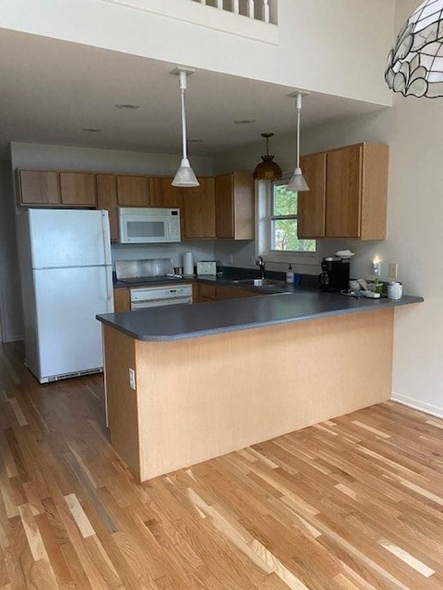 kitchen featuring kitchen peninsula, white appliances, decorative light fixtures, and light hardwood / wood-style floors