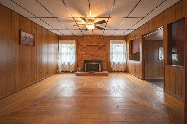 unfurnished living room featuring a wood stove, ceiling fan, and wood walls