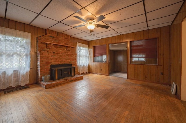 unfurnished living room featuring a drop ceiling, light hardwood / wood-style flooring, ceiling fan, and wooden walls