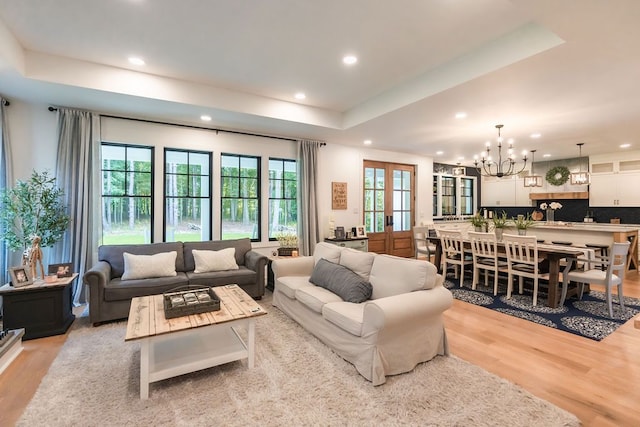 living room featuring an inviting chandelier, a raised ceiling, french doors, and light hardwood / wood-style flooring