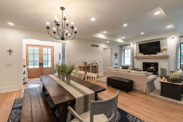 dining room with a fireplace, french doors, light wood-type flooring, and a healthy amount of sunlight