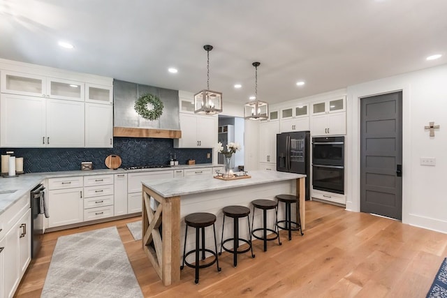 kitchen featuring white cabinetry, a center island, a kitchen breakfast bar, black appliances, and light wood-type flooring