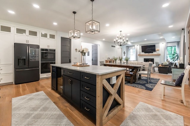 kitchen featuring black appliances, white cabinets, hanging light fixtures, light wood-type flooring, and a kitchen island