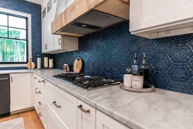 kitchen with appliances with stainless steel finishes, premium range hood, light stone counters, light hardwood / wood-style flooring, and white cabinetry