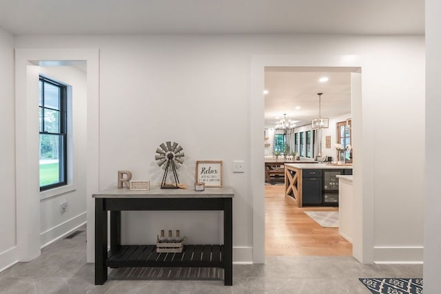 hallway featuring light wood-type flooring, beverage cooler, and a chandelier