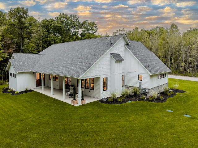 back house at dusk featuring a yard and a patio