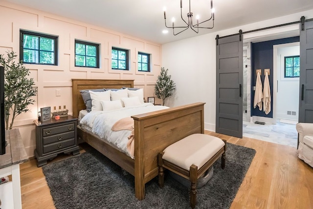 bedroom with a barn door, light hardwood / wood-style flooring, and a notable chandelier