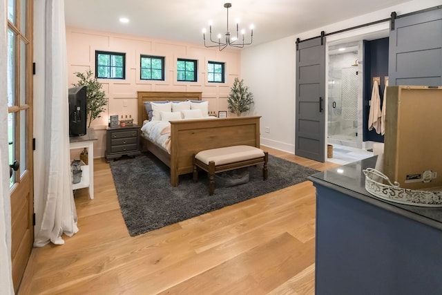 bedroom featuring a chandelier, a barn door, connected bathroom, and light hardwood / wood-style flooring