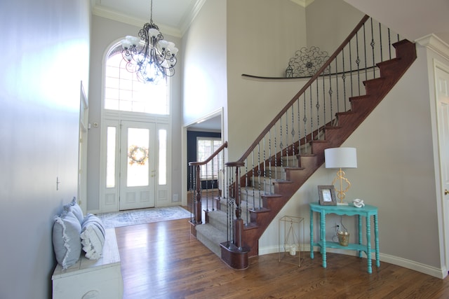 foyer entrance featuring wood-type flooring, crown molding, a high ceiling, and a chandelier