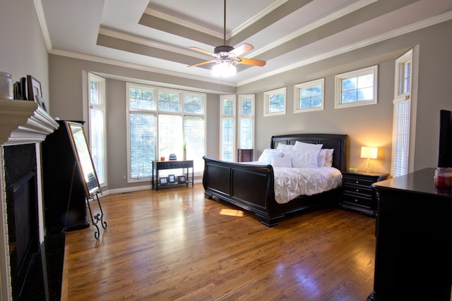 bedroom with hardwood / wood-style flooring, ceiling fan, crown molding, and a tray ceiling