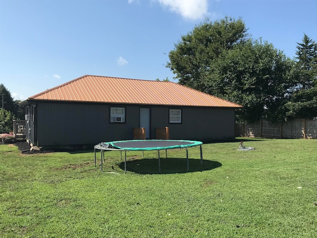 back of property with a trampoline and a yard