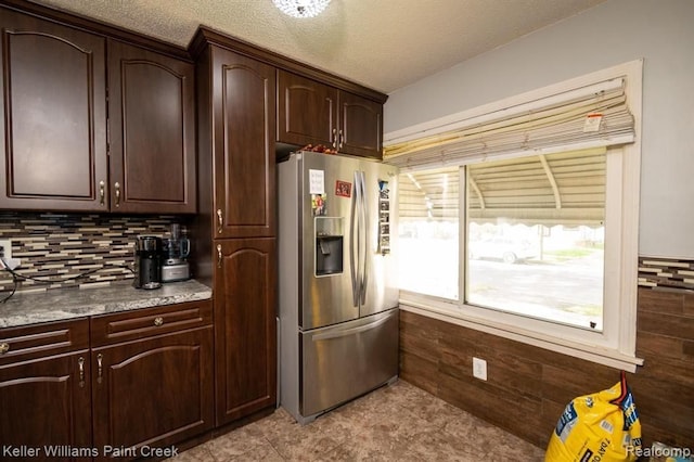 kitchen featuring a textured ceiling, decorative backsplash, dark brown cabinets, and stainless steel refrigerator with ice dispenser