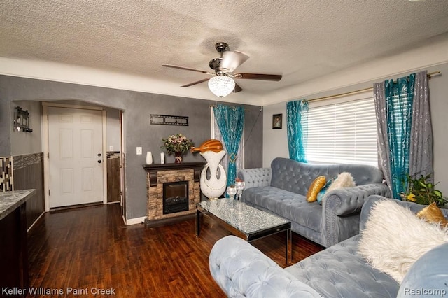 living room featuring a fireplace, a textured ceiling, dark hardwood / wood-style floors, and ceiling fan