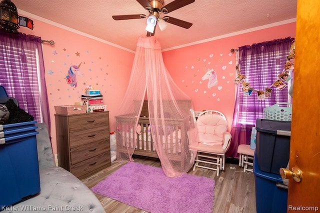 bedroom featuring hardwood / wood-style floors, a textured ceiling, a nursery area, and crown molding