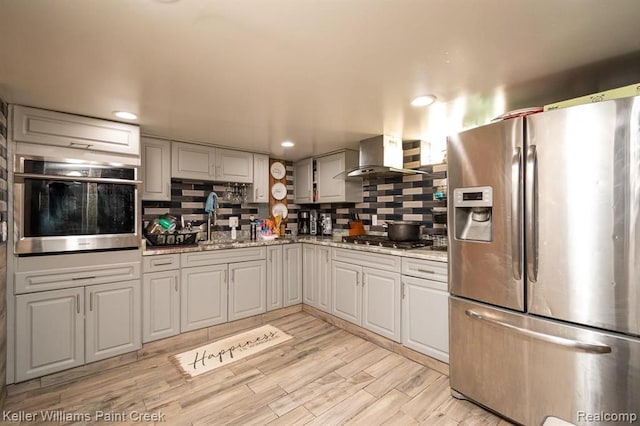 kitchen with tasteful backsplash, wall chimney exhaust hood, stainless steel appliances, and light wood-type flooring