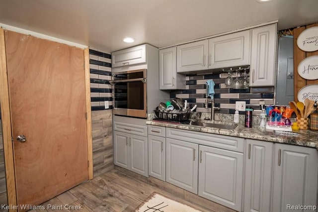 kitchen with white cabinets, oven, sink, dark stone countertops, and light wood-type flooring