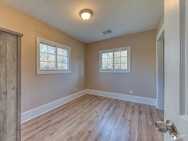 unfurnished bedroom featuring light hardwood / wood-style floors, a textured ceiling, and multiple windows