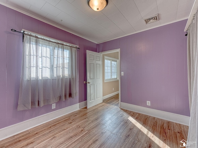 spare room featuring light hardwood / wood-style flooring, ornamental molding, and wood walls