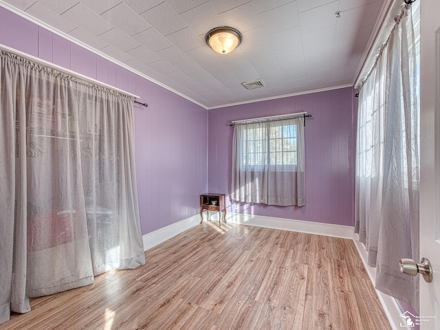 empty room featuring ornamental molding, wooden walls, and light hardwood / wood-style flooring