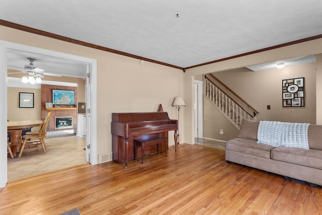 living room with ceiling fan, light wood-type flooring, ornamental molding, and a brick fireplace