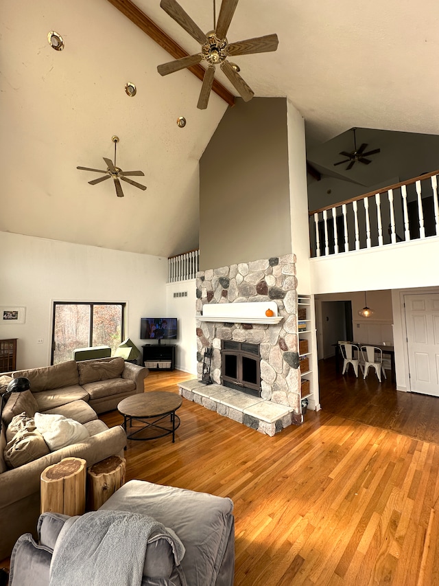 living room with a stone fireplace, beamed ceiling, high vaulted ceiling, and wood-type flooring