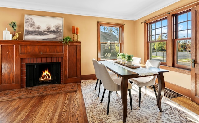 dining area featuring a brick fireplace, light hardwood / wood-style flooring, and crown molding