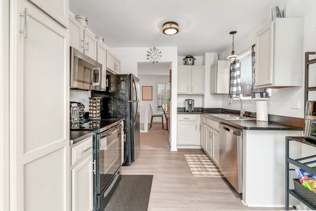 kitchen featuring light wood-type flooring, stainless steel appliances, sink, decorative light fixtures, and white cabinets