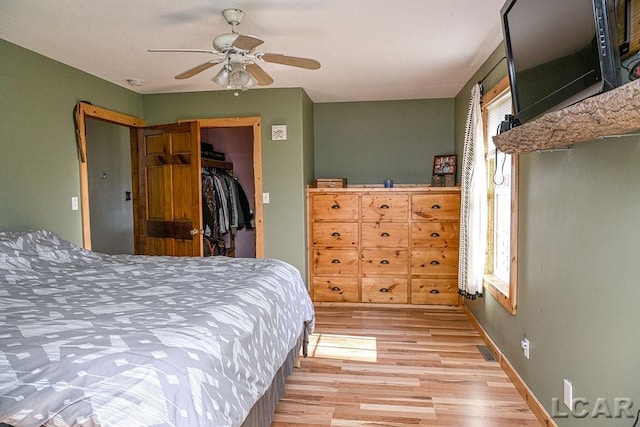 bedroom with light wood-type flooring, a closet, a spacious closet, and ceiling fan