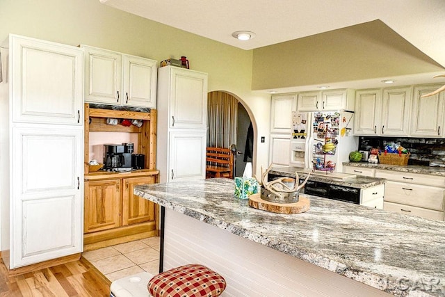 kitchen featuring decorative backsplash, light stone countertops, white fridge with ice dispenser, and light wood-type flooring