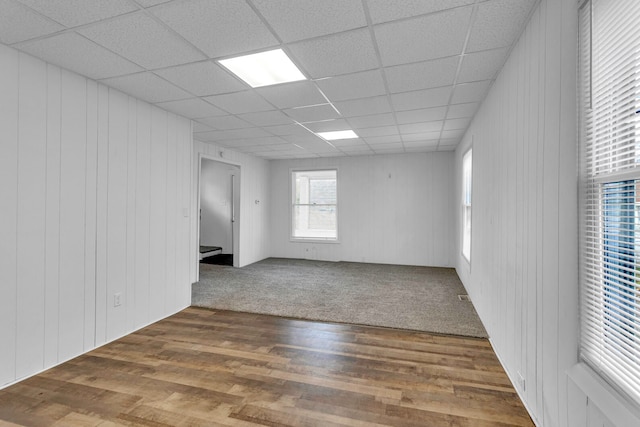 unfurnished room featuring hardwood / wood-style floors, a drop ceiling, and wooden walls