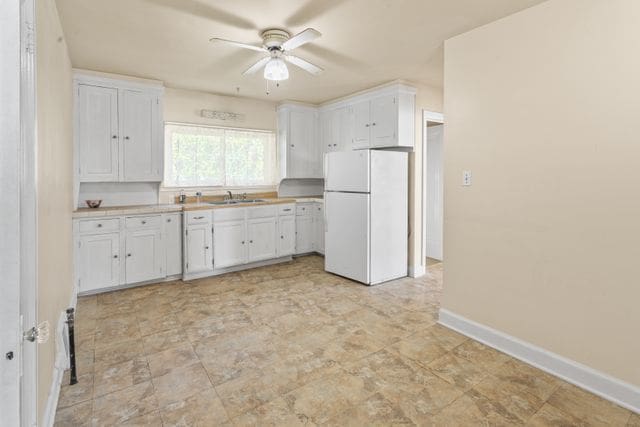 kitchen featuring white cabinets, white fridge, ceiling fan, and sink