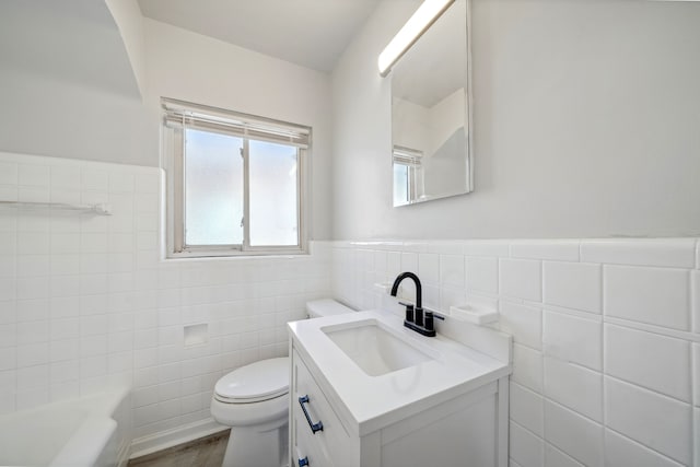 bathroom featuring a washtub, vanity, tile walls, hardwood / wood-style floors, and toilet