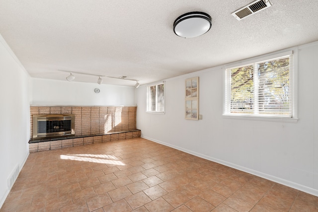 unfurnished living room featuring a textured ceiling, a brick fireplace, and plenty of natural light