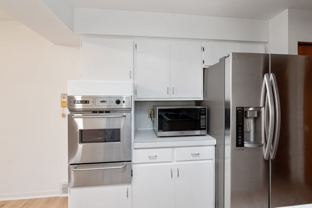 kitchen with white cabinets, appliances with stainless steel finishes, and light hardwood / wood-style flooring