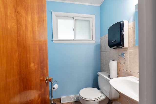 bathroom with toilet, sink, ornamental molding, and tile walls