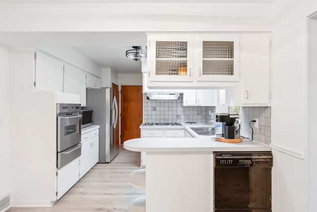 kitchen featuring appliances with stainless steel finishes, backsplash, extractor fan, light hardwood / wood-style floors, and white cabinetry