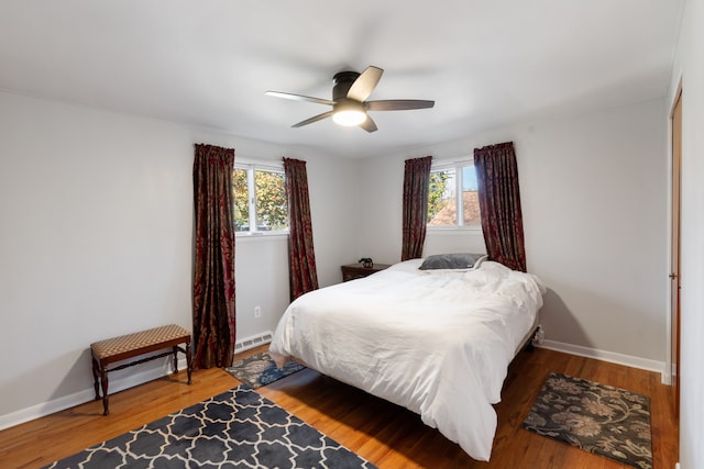 bedroom with hardwood / wood-style floors, baseboard heating, multiple windows, and ceiling fan