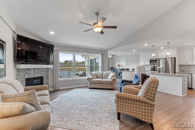 living room featuring a stone fireplace, ceiling fan, high vaulted ceiling, and light wood-type flooring