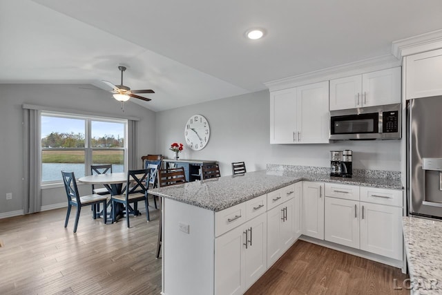 kitchen with white cabinetry, stainless steel appliances, kitchen peninsula, wood-type flooring, and lofted ceiling