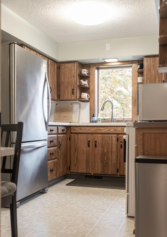 317 Maiden Ln, Saint Joseph, MI 49085 - kitchen featuring freestanding refrigerator, open shelves, brown cabinets, a textured ceiling, and light countertops