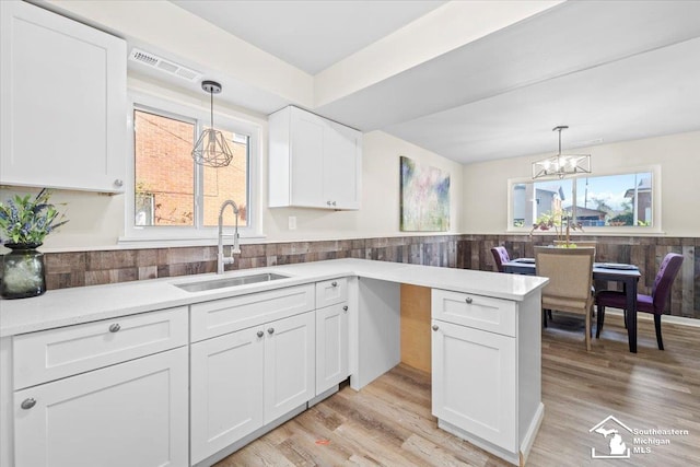 kitchen with decorative light fixtures, light hardwood / wood-style floors, white cabinetry, and sink